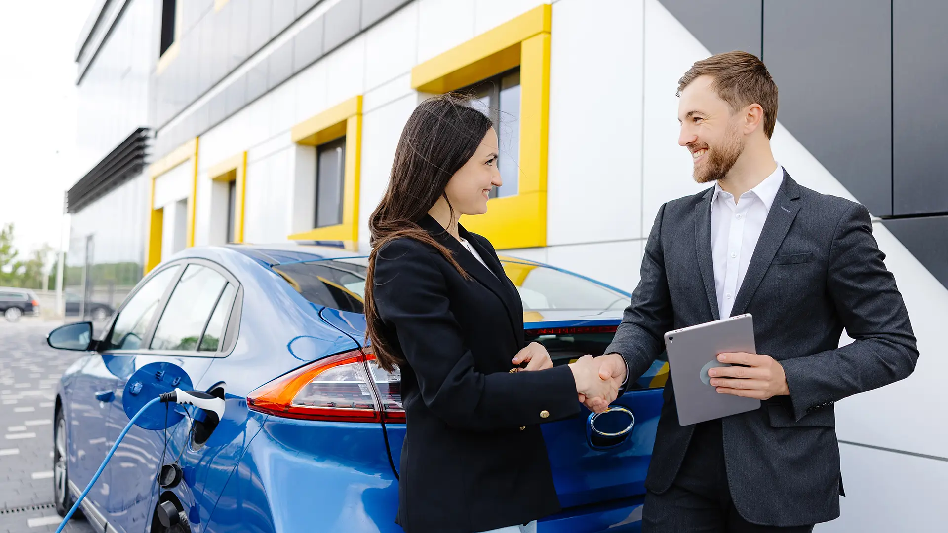 Smiling woman standing at the car and pointing at car seller tablet. She is picked right car for her she saw online