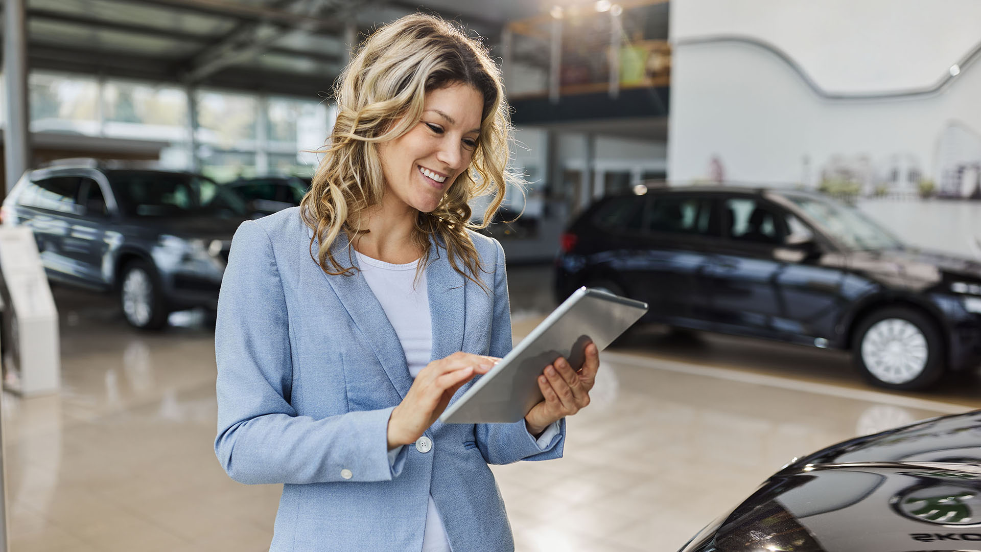 Happy car salesperson using digital tablet in a showroom